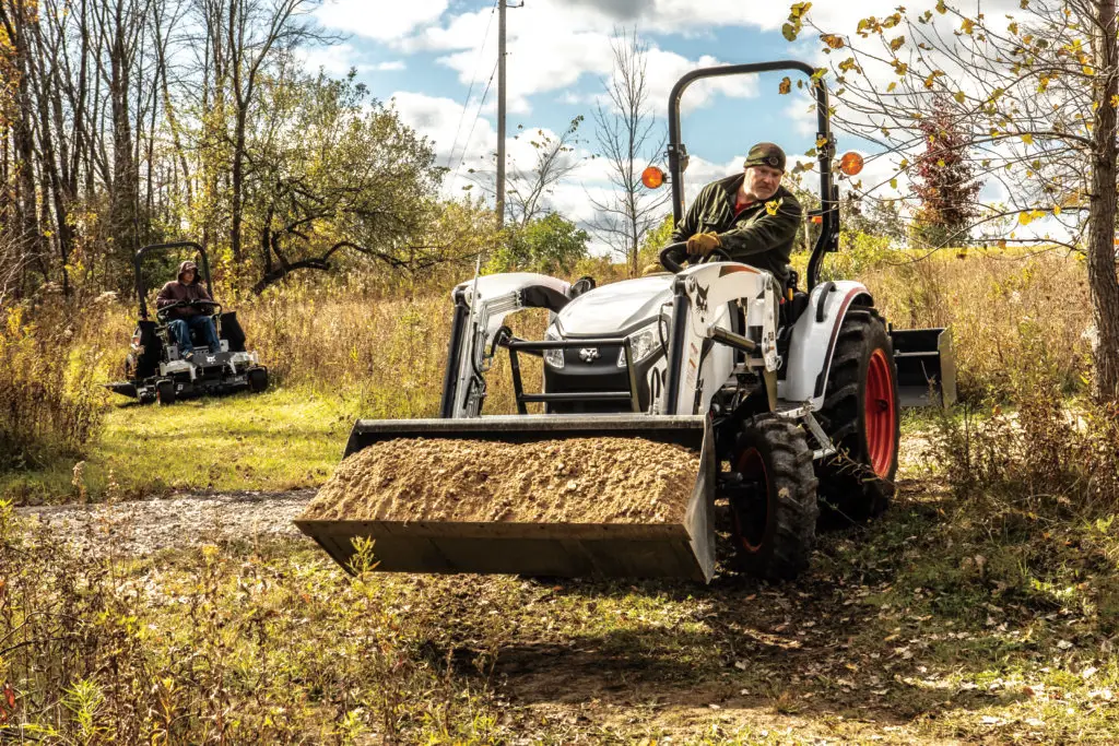 Bobcat tractor with a front end loader hauling dirt.